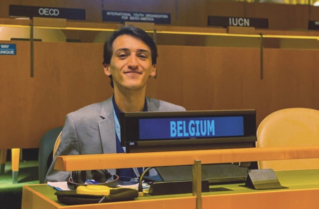 Hasan Jashari, wearing a gray suit over a black sweater, sits at a wooden desk in the UN chamber. In front of him is a digital screen that reads "Belgium" in blue text.