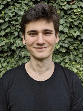 Hamza Hashem, wearing a black t-shirt, poses for a photo in front of a leafy green backdrop.