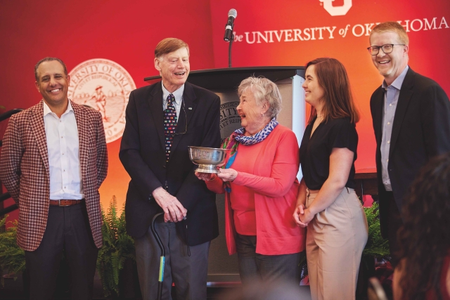 On stage in front of a red wall, OU President Joseph Harroz, Jr , Phil Geier, JoAnn Holden, Emelie Schultz, and Craig Hayes stand together to celebrate the Davis cup win.