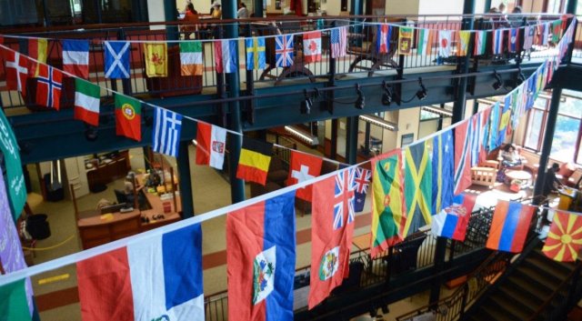 Criss-crossing ropes display a multitude of international flags, all hanging above an open stairwell.